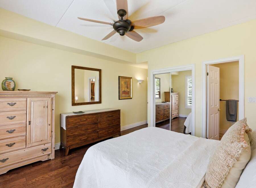 This spacious bedroom features a light yellow paint scheme, complemented by a dark wood floor and a ceiling fan for optimal comfort.