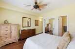 This spacious bedroom features a light yellow paint scheme, complemented by a dark wood floor and a ceiling fan for optimal comfort.