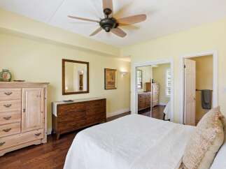 This spacious bedroom features a light yellow paint scheme, complemented by a dark wood floor and a ceiling fan for optimal comfort.