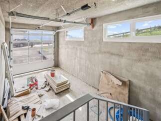 This unfinished garage space offers a fantastic opportunity for customization, featuring a modern sectional garage door with glass panels and two large windows that allow ample natural light.