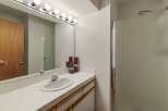 This bathroom features a spacious vanity with a tiled countertop and a large mirror illuminated by a vanity light fixture.