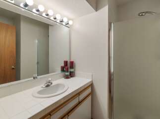 This bathroom features a spacious vanity with a tiled countertop and a large mirror illuminated by a vanity light fixture.