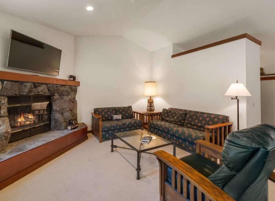 Cozy up by the stone fireplace in this inviting living room, featuring comfortable seating and a large flat-screen TV for entertainment.