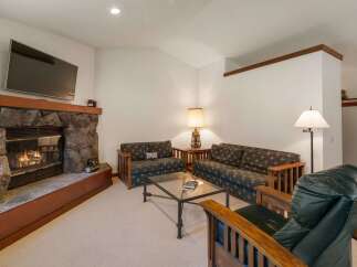 Cozy up by the stone fireplace in this inviting living room, featuring comfortable seating and a large flat-screen TV for entertainment.