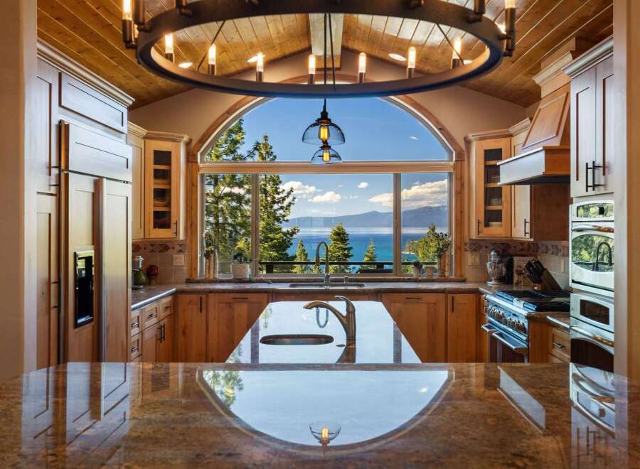 Experience breathtaking lake views from this stunning kitchen, featuring a large arched window framing the serene waters and surrounding mountains.