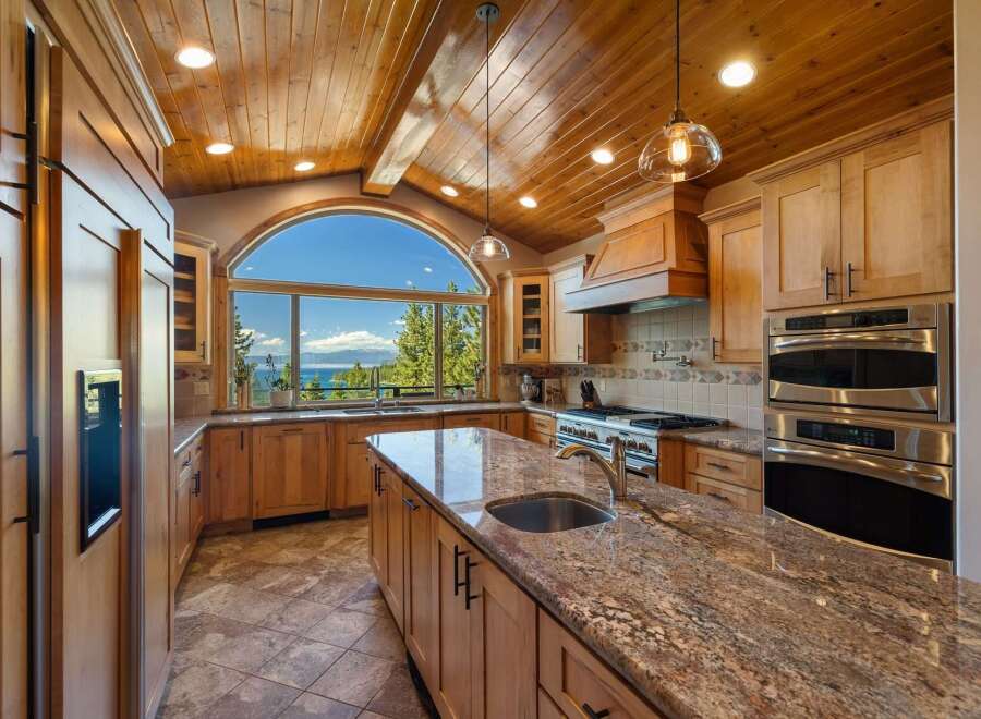 Experience luxury living in this stunning kitchen featuring a large granite island with a sink and a breathtaking arched window offering panoramic lake and mountain views.