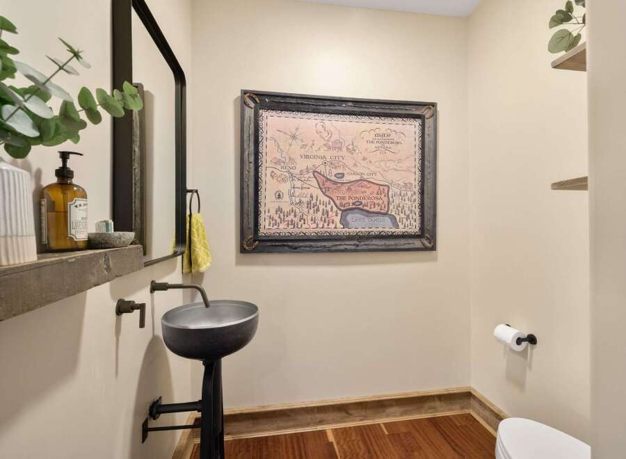 This charming powder room features a unique industrial-style pedestal sink and a rustic wooden shelf displaying a decorative soap dispenser and eucalyptus.