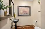 This charming powder room features a unique industrial-style pedestal sink and a rustic wooden shelf displaying a decorative soap dispenser and eucalyptus.
