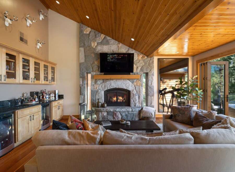 Experience luxury mountain living in this stunning great room, featuring a grand stone fireplace and a vaulted wood-paneled ceiling.