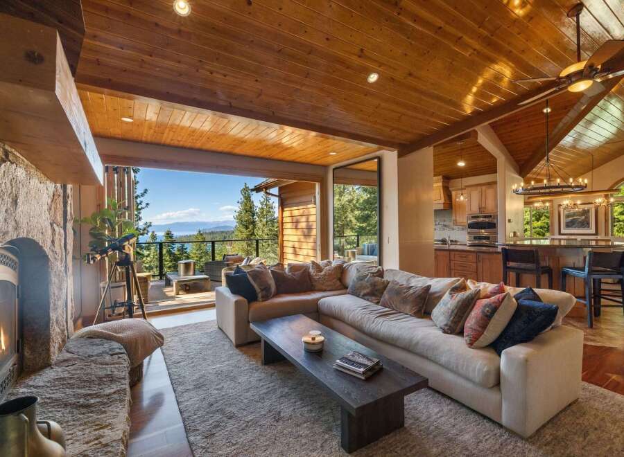 Experience breathtaking lake and mountain views from this stunning living room, featuring a cozy stone fireplace and expansive sliding glass doors that open to a scenic deck.