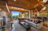 Experience breathtaking lake and mountain views from this stunning living room, featuring a cozy stone fireplace and expansive sliding glass doors that open to a scenic deck.