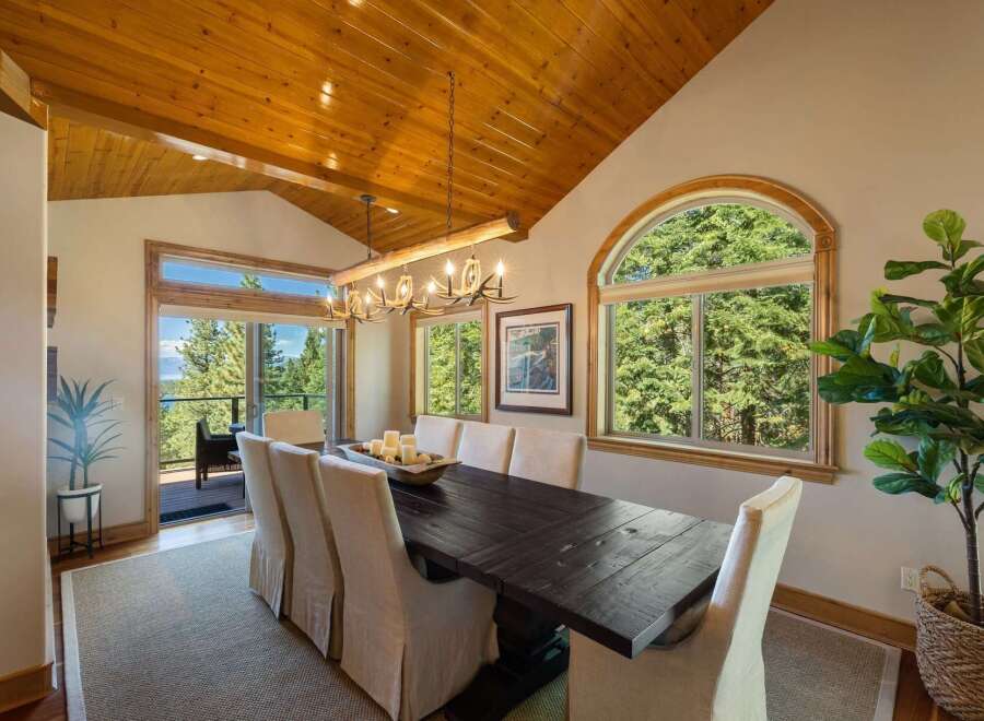 Experience breathtaking views from this stunning dining room, featuring a rustic antler chandelier and a large wooden table perfect for gatherings.