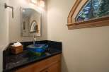 This powder room features a striking blue and green glass vessel sink atop a black granite countertop, complemented by warm wooden cabinetry.