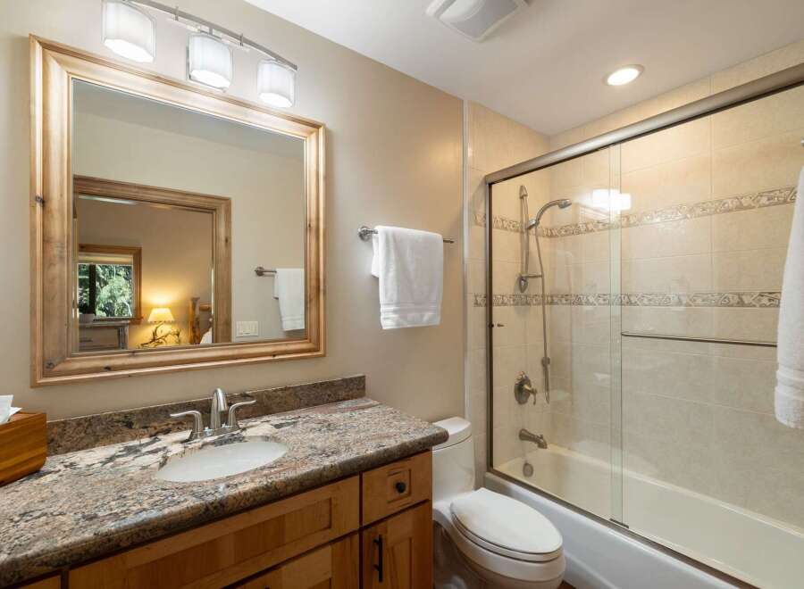 This charming bathroom features a spacious vanity with a granite countertop and a wooden cabinet, complemented by a large wooden-framed mirror.