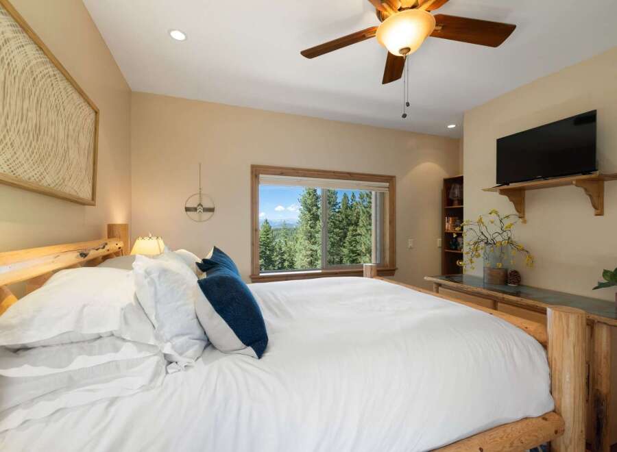 Experience breathtaking mountain views from this serene bedroom, featuring a comfortable king-size bed and a large window overlooking a lush forest.