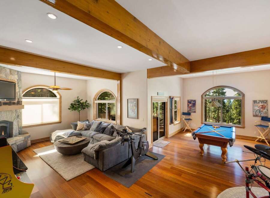 Experience ultimate relaxation and entertainment in this spacious living area, featuring a cozy sectional sofa, a stone fireplace, and a dedicated game room with a pool table and arcade machine.