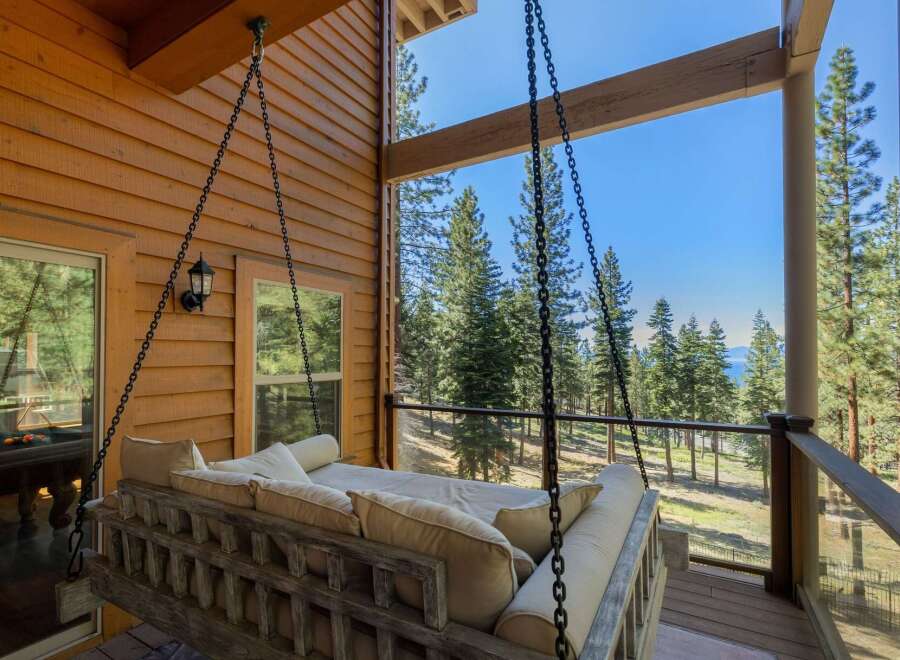 Experience ultimate relaxation on this charming porch swing, offering breathtaking views of lush pine trees and a distant lake.