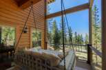 Experience ultimate relaxation on this charming porch swing, offering breathtaking views of lush pine trees and a distant lake.