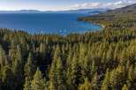 Experience the ultimate lakeside living with this stunning aerial view of a property nestled amidst a dense pine forest, offering breathtaking vistas of a crystal-clear blue lake.