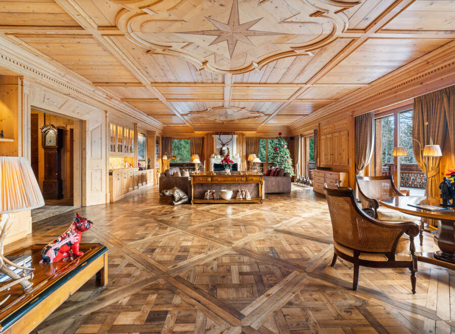 Experience unparalleled luxury in this stunning wood-paneled living room, featuring an intricate coffered ceiling with a compass rose inlay and a grand fireplace.