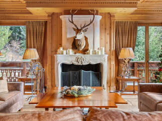 Experience rustic luxury in this charming living room, featuring a grand stone fireplace adorned with a majestic deer mount and surrounded by warm wood paneling.