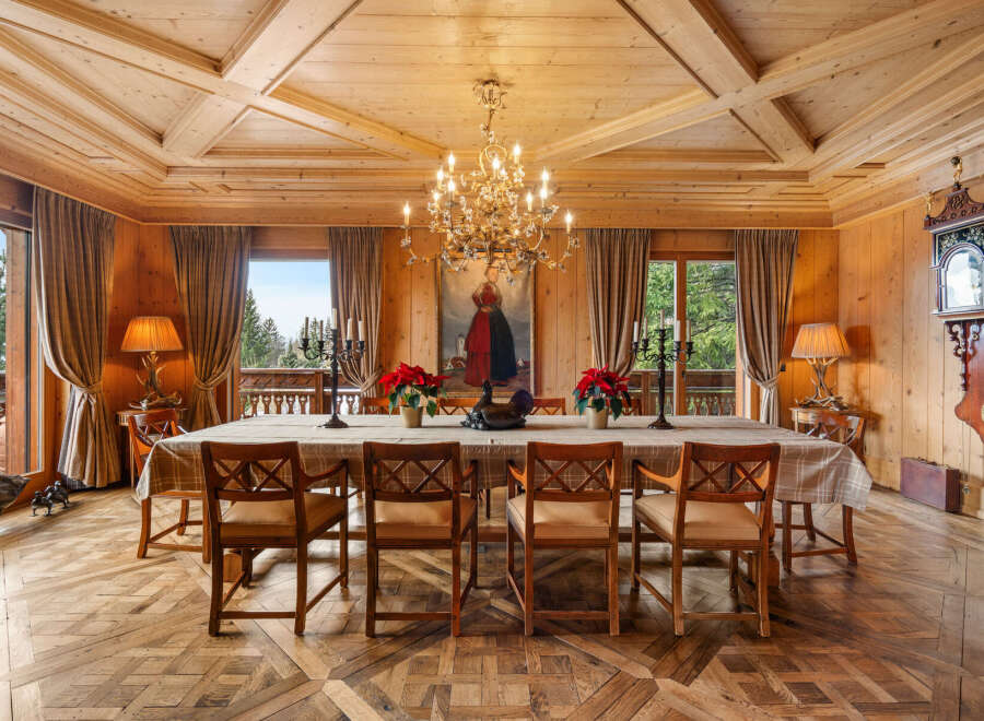 Experience rustic elegance in this stunning dining room, featuring a grand wooden table set for a feast under a magnificent chandelier.