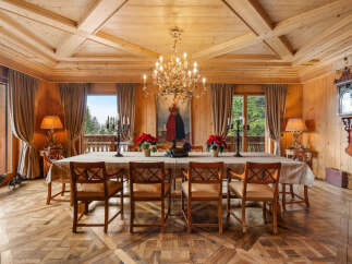 Experience rustic elegance in this stunning dining room, featuring a grand wooden table set for a feast under a magnificent chandelier.