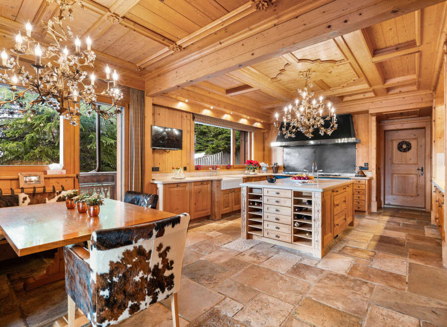 Experience rustic luxury in this charming wooden kitchen, featuring a large dining table with unique cowhide chairs and ornate chandeliers.