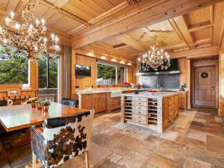 Experience rustic luxury in this charming wooden kitchen, featuring a large dining table with unique cowhide chairs and ornate chandeliers.