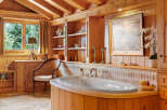 Experience ultimate relaxation in this luxurious wooden bathroom, featuring a deep soaking tub with stunning forest views.