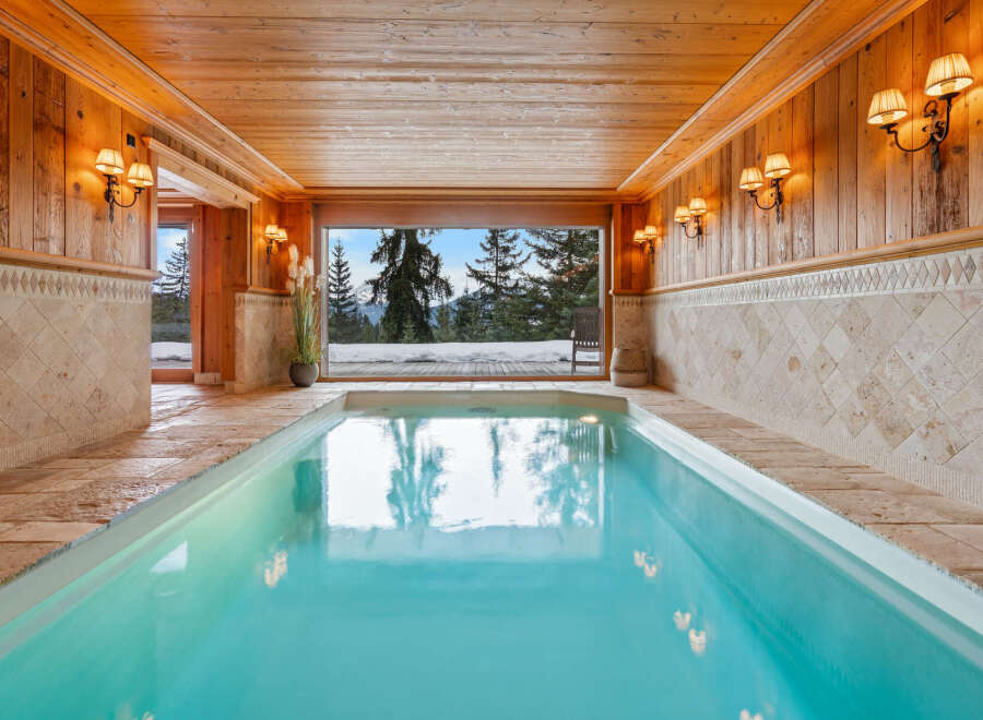 Experience ultimate relaxation in this indoor swimming pool, featuring a stunning panoramic view of a snowy mountain landscape.