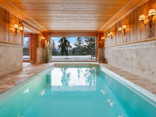 Experience ultimate relaxation in this indoor swimming pool, featuring a stunning panoramic view of a snowy mountain landscape.