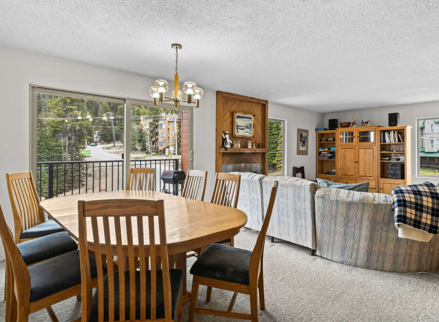 Enjoy mountain views from this spacious dining and living area, featuring a large wooden dining table with chairs and a cozy living room with a fireplace and entertainment center.