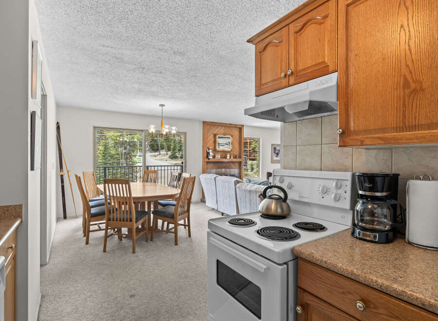 Experience comfortable living in this inviting space, featuring a well-appointed kitchen with a stove and coffee maker, adjacent to a dining area with a round wooden table and chairs.