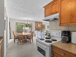 Experience comfortable living in this inviting space, featuring a well-appointed kitchen with a stove and coffee maker, adjacent to a dining area with a round wooden table and chairs.