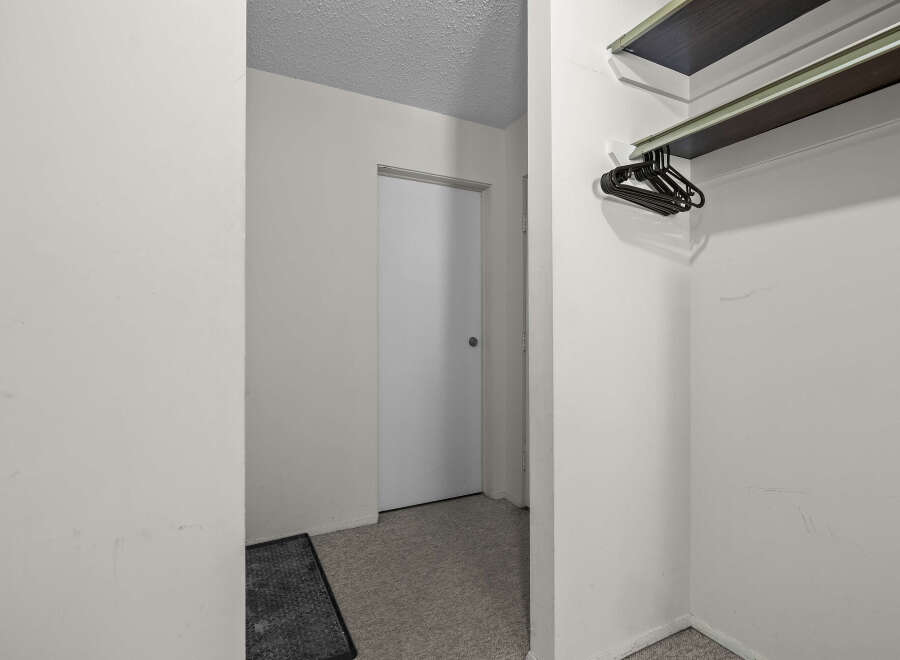 Discover ample storage solutions in this property, featuring a convenient closet with a built-in shelf and a rack of black hangers.