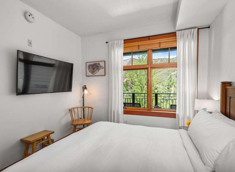 Experience breathtaking mountain views from this serene bedroom, featuring a large window overlooking lush greenery and rolling hills.