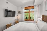 Experience breathtaking mountain views from this serene bedroom, featuring a large window overlooking lush greenery and rolling hills.