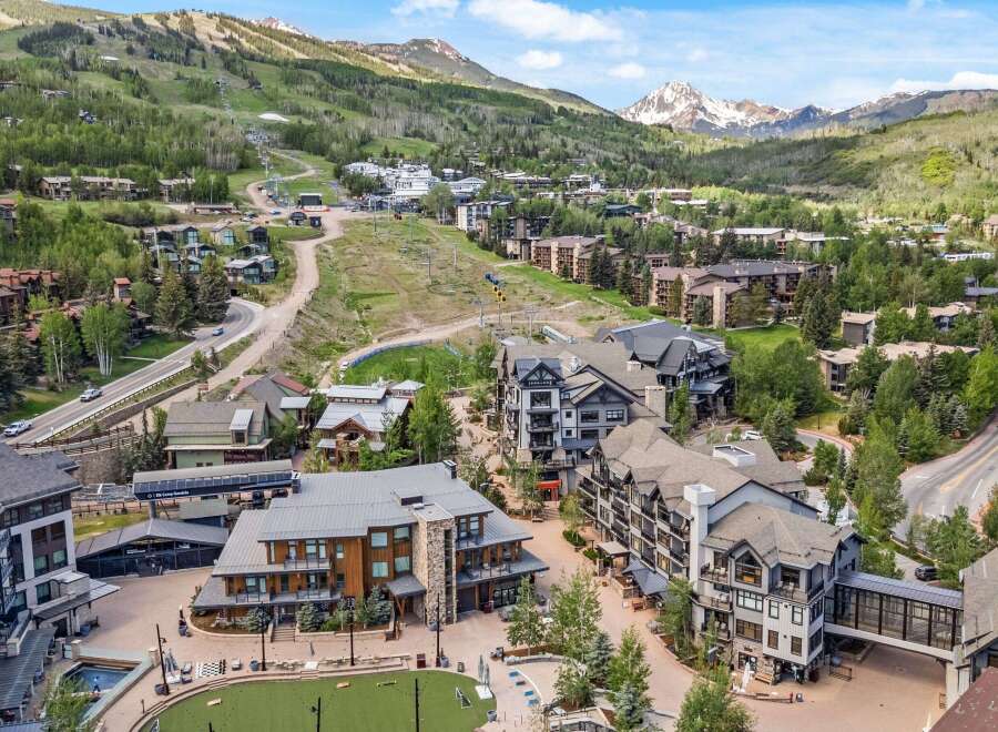 Experience luxury mountain living in this stunning ski resort village, featuring modern architecture nestled amidst lush green slopes and majestic peaks.