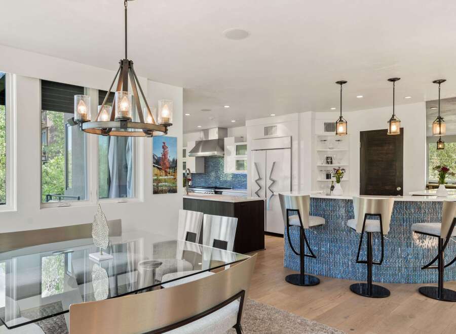 Experience modern luxury in this open-concept living space, featuring a sleek glass dining table and a stunning blue tiled kitchen island with bar seating.