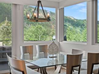 Experience breathtaking mountain views from this elegant dining room, featuring a sleek glass-top table and modern chairs.