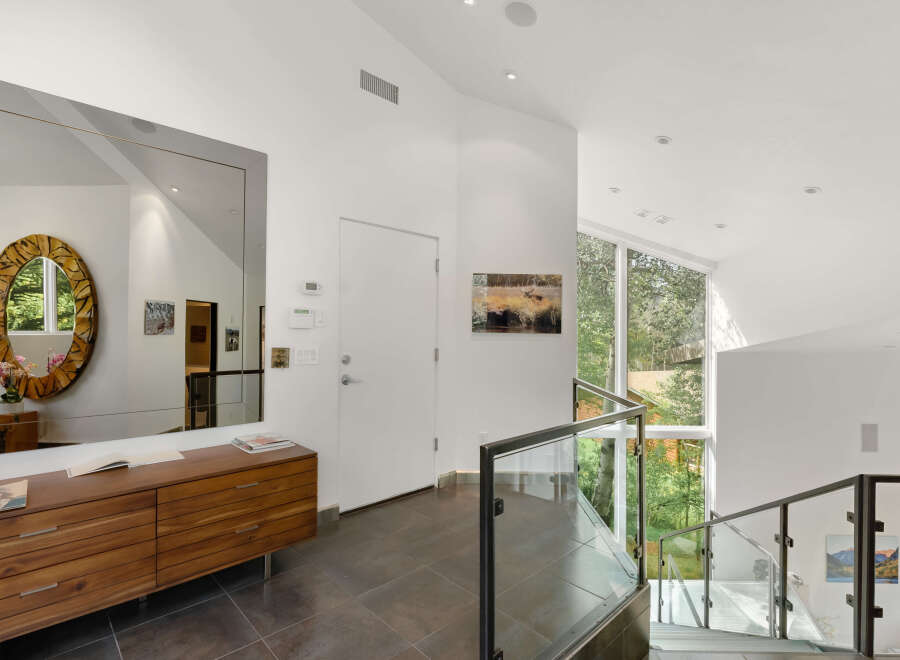 This modern entryway features a large, ornate mirror reflecting the natural light pouring in from the expansive windows.