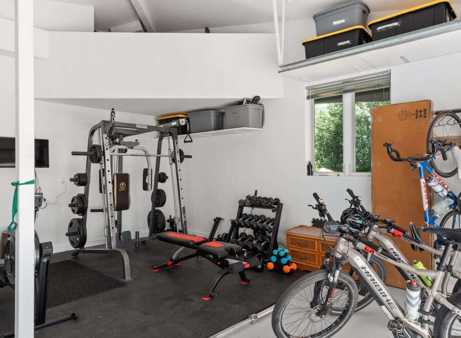 This spacious garage offers a dedicated home gym area with a Marcy weight machine, adjustable bench, and a full set of dumbbells, perfect for your fitness routine.
