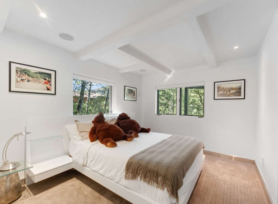 This bright and airy bedroom features a modern white platform bed adorned with two large teddy bears and a cozy knit throw.