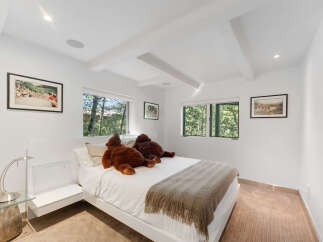 This bright and airy bedroom features a modern white platform bed adorned with two large teddy bears and a cozy knit throw.