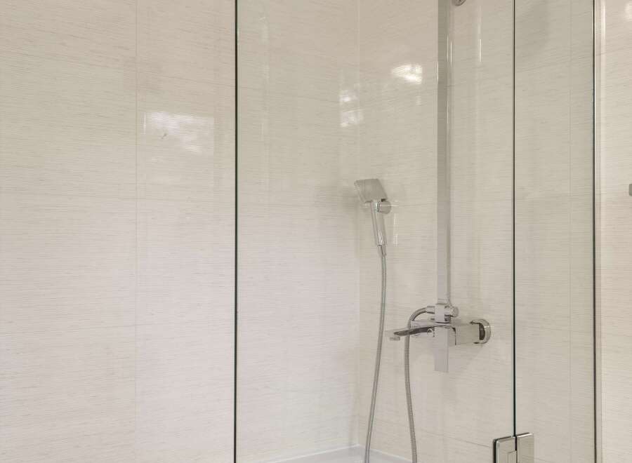 Experience modern elegance in this bathroom featuring a sleek glass shower enclosure over a pristine white bathtub.