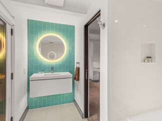 Experience modern luxury in this stunning bathroom, featuring a vibrant teal tiled accent wall with a backlit circular mirror.