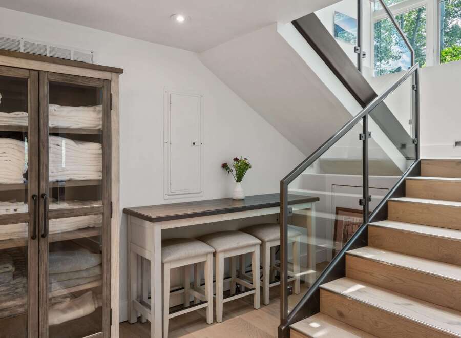This modern interior features a sleek staircase with glass railings and natural wood steps, leading to a bright upper level.