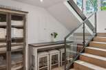 This modern interior features a sleek staircase with glass railings and natural wood steps, leading to a bright upper level.