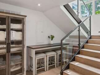 This modern interior features a sleek staircase with glass railings and natural wood steps, leading to a bright upper level.